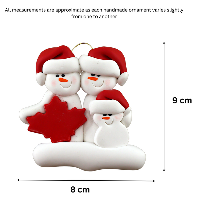 Family ornament with 3 white snowmen in red hats, gathered around a red maple leaf, graphed to show size (8x9cm).