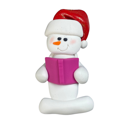 Ornament of white snowman in red hat holding a pink book.