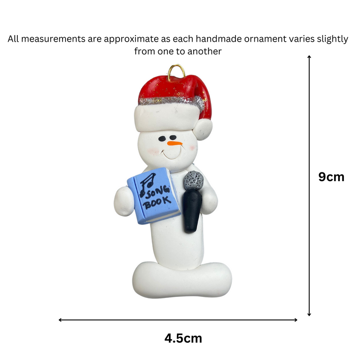 Ornament of white snowman in red hat holding a microphone and blue music book, graphed to show size (4.5x9cm).