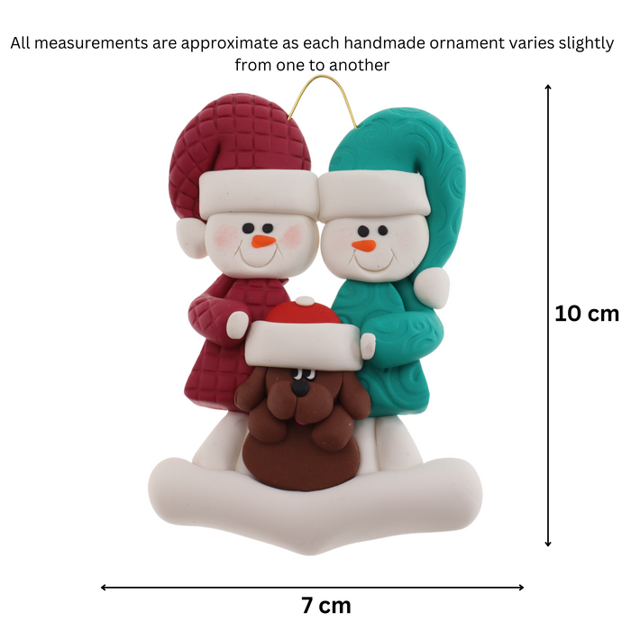 Ornament of snowman couple in red and green shirts and hats with brown dog in Christmas hat, graphed to show size (7x10cm).
