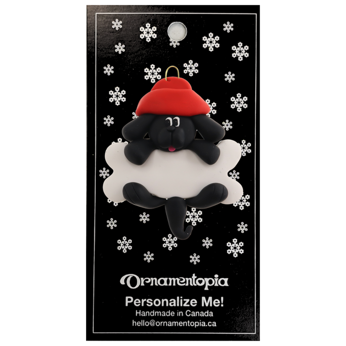 Ornament of black dog in red hat hanging on a white bone, on display backing card.