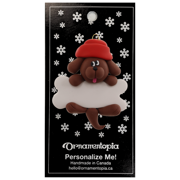 Ornament of brown dog in red hat hanging on a white bone, on display backing card.
