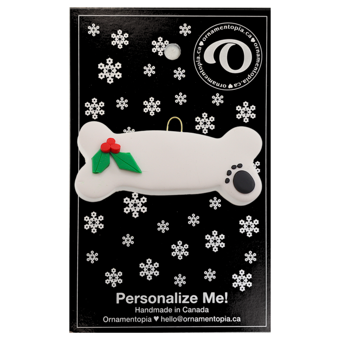 Ornament of dog bone with holly and paw print, on display backing card.