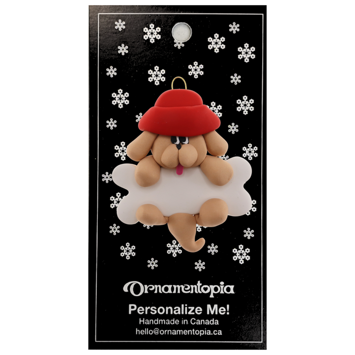Ornament of tan dog in red hat hanging on a white bone, on display backing card.
