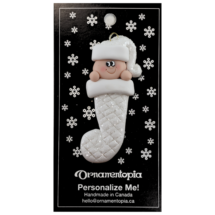 Ornament with infant head in a white glitter hat poking out of a white glitter stocking, on display backing card.