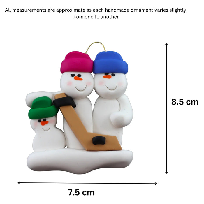 Family ornament with 3 white snowmen in bright hats, holding a hockey stick, graphed to show size (7.5x8.5cm).