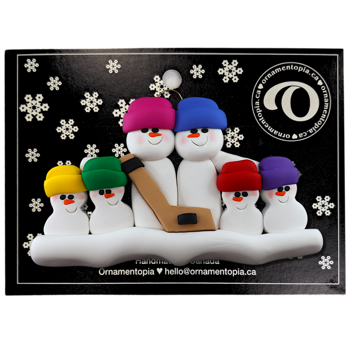 Family ornament with 6 white snowmen in bright hats, holding a hockey stick, on display backing card.