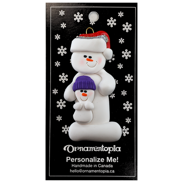 Ornament of white snowman in red hat holding smaller snowman, on display backing card.