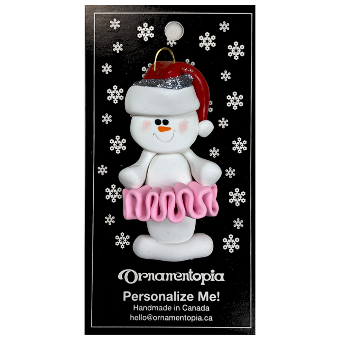 Ornament of white snowman in red hat wearing a pink tutu, on display backing card.
