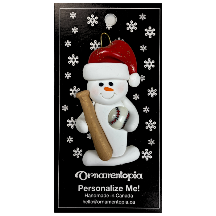 Ornament of white snowman in red hat holding a baseball bat and a baseball, on display backing card.
