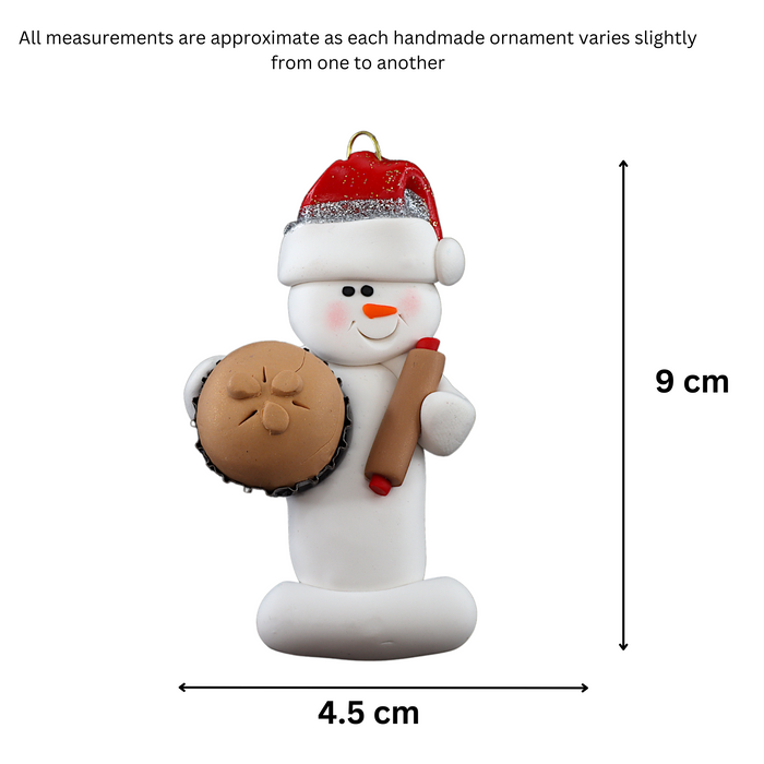 Ornament of white snowman in red hat holding a baked pie and rolling pin, graphed to show size (4.5x9cm).