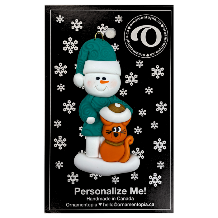 Ornament of snowman in a green shirt and hat with orange cat in Christmas hat, on display backing card.
