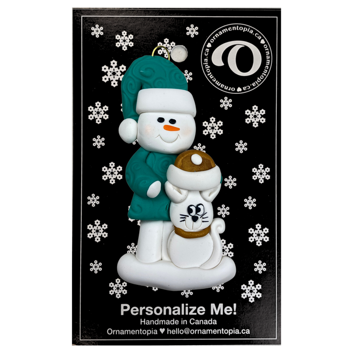 Ornament of snowman in a green shirt and hat with white cat in Christmas hat, on display backing card.