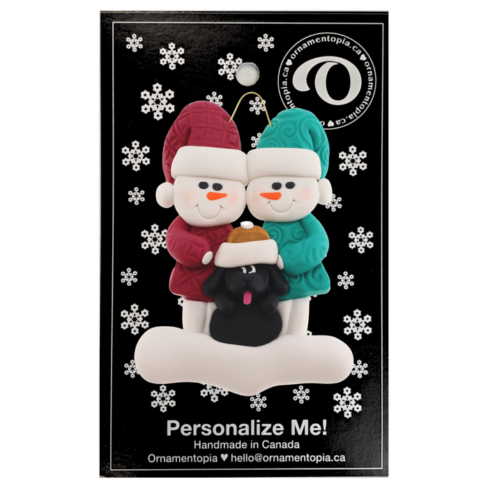 Ornament of snowman couple in red and green shirts and hats with black dog in Christmas hat, on display backing card.