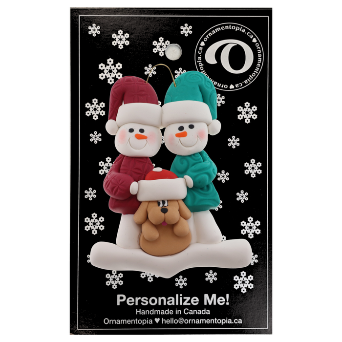 Ornament of snowman couple in red and green shirts and hats with tan dog in Christmas hat, on display backing card.