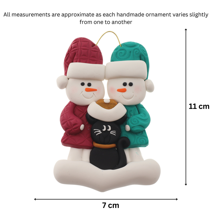 Ornament of snowman couple in red and green shirts and hats with a black cat in Christmas hat, graphed to show size (7x11cm).