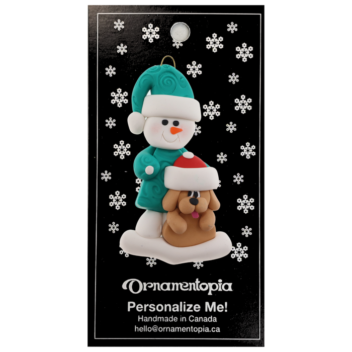 Ornament of snowman in green shirt and hat with tan dog in Christmas hat, on display backing card.