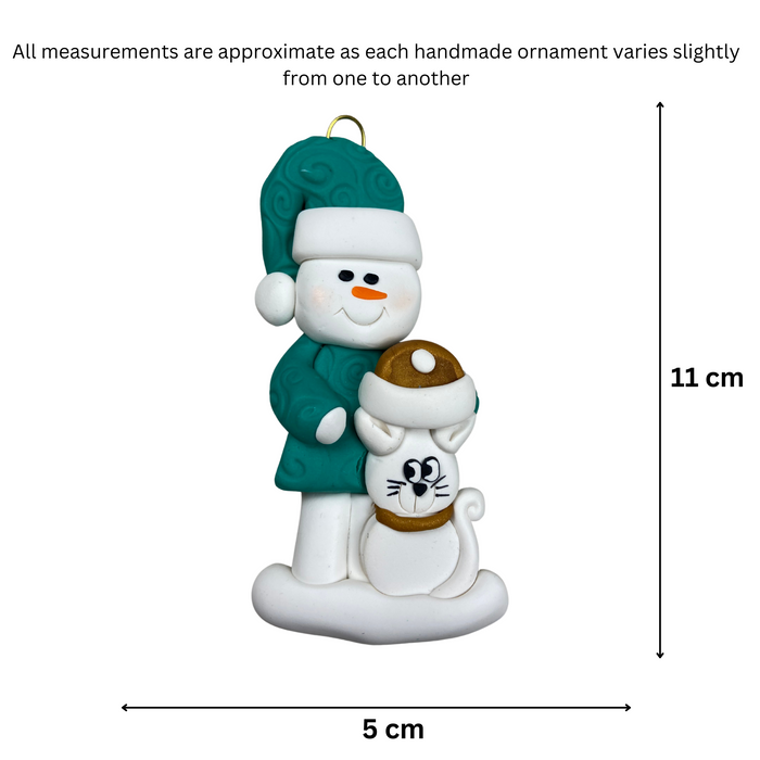 Ornament of snowman in a green shirt and hat with white cat in Christmas hat, graphed to show size (5x11cm).