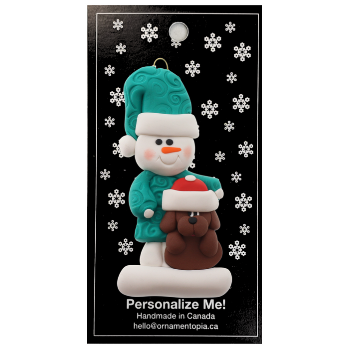 Ornament of snowman in green shirt and hat with brown dog in Christmas hat, on display backing card.