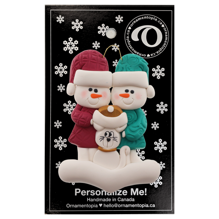 Ornament of snowman couple in red and green shirts and hats with a white cat in Christmas hat, on a display backing card.