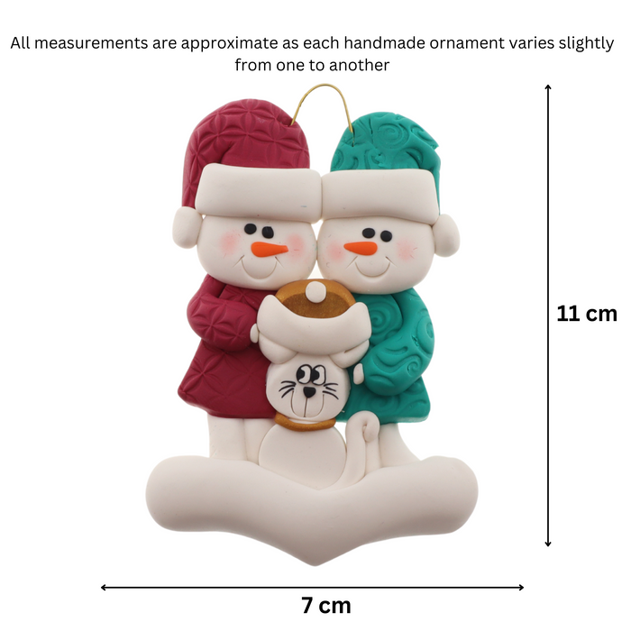 Ornament of snowman couple in red and green shirts and hats with a white cat in Christmas hat, graphed to show size (7x11cm).